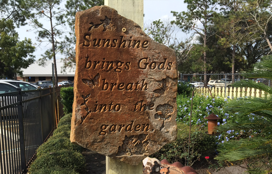 A memorial stone with etched words 'Sunshine brings Gods breath into the garden'.