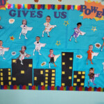 A self-made board with a city in the background and tiny figures of supermen with kids faces clipped on top and a sign 'God Gives Us Power'.