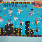 A self-made board with a city in the background and tiny figures of supermen with kids faces clipped on top and a sign 'God Gives Us Power'.