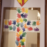 A self-made paper cross with colored hand prints on top and a sign 'He Saves Us' above a superman logo with J inside instead of S.