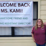 Sign 'Welcome back Ms. Kami!' with two female staff standing next to it.